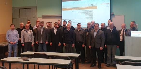 A group of men standing in front of a projector screenDescription generated with high confidence